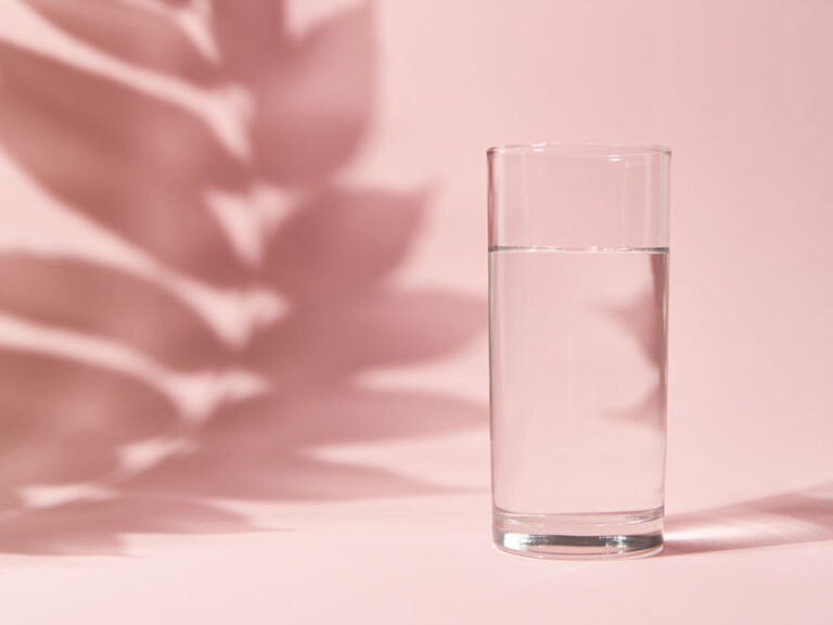 Half a glass of water on pink background