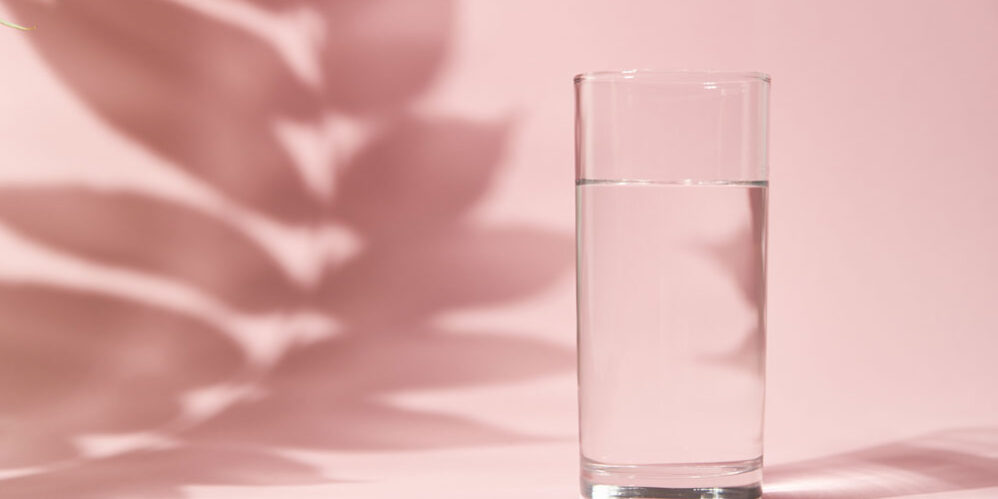 Half a glass of water on pink background