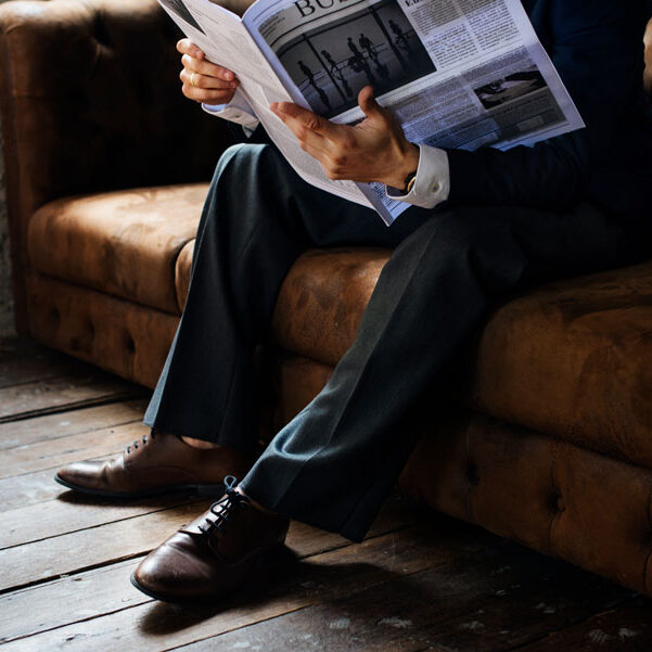 Man reading the newspaper on the a brown couch.
