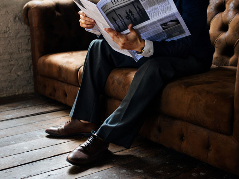 Man reading the newspaper on the a brown couch.