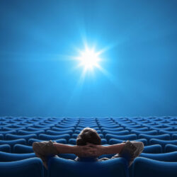 Man from behind sitting in an empty theater looking at a blue screen.