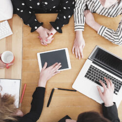 Birds eye view of group of business with only their hands and computers showing collabrating together.