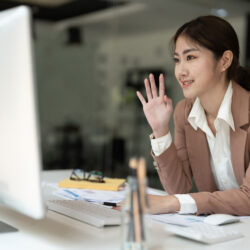Young Asian business woman waving into computer.